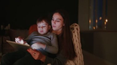 Güzel kadın anne evine oğlu ile çizgi tablet dokunmatik ekranda izlerken onun kucağına bir sandalyede oturuyor.