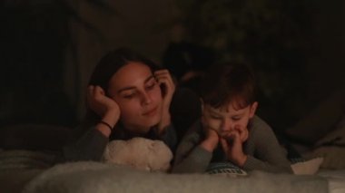 Mutlu aile anne ve oğlu tablet ekran oyun evinin yatak odasında yatağın üstüne yalan