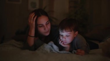 Mutlu aile anne ve oğlu tablet ekran oyun evinin yatak odasında yatağın üstüne yalan