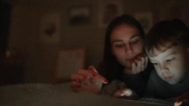 Mutlu aile anne ve oğlu tablet ekran oyun evinin yatak odasında yatağın üstüne yalan