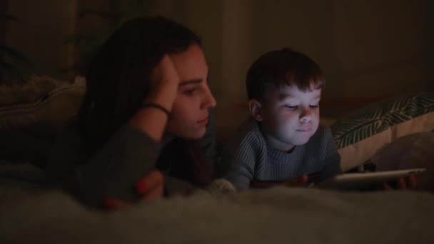 Família feliz mãe e filho deitado na cama no quarto de sua casa jogando jogos na tela do tablet — Vídeo de Stock