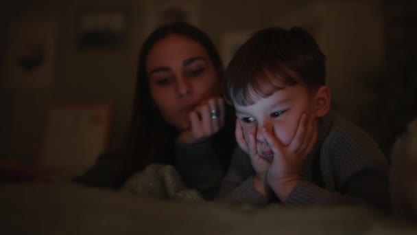 Família feliz mãe e filho deitado na cama no quarto de sua casa jogando jogos na tela do tablet — Vídeo de Stock