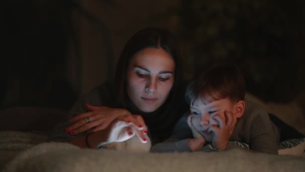 Glückliche Familienmutter und Sohn liegen auf dem Bett im Schlafzimmer seines Hauses und spielen Spiele auf dem Bildschirm des Tablets — Stockvideo