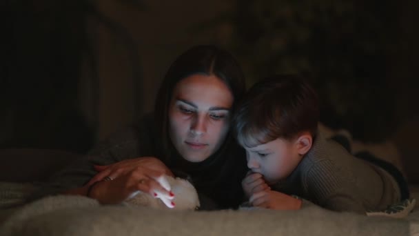 Glückliche Familienmutter und Sohn liegen auf dem Bett im Schlafzimmer seines Hauses und spielen Spiele auf dem Bildschirm des Tablets — Stockvideo