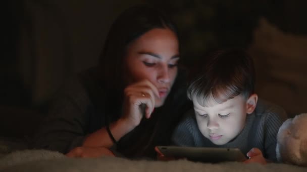 幸せな家族母と息子タブレットの画面のゲームをプレイする彼の家の寝室のベッドの上に横たわる — ストック動画