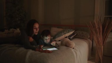 Mutlu aile anne ve oğlu tablet ekran oyun evinin yatak odasında yatağın üstüne yalan