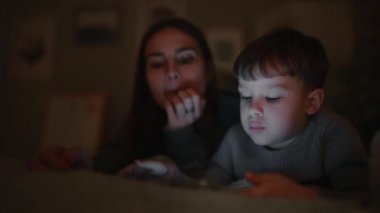 Mutlu aile anne ve oğlu tablet ekran oyun evinin yatak odasında yatağın üstüne yalan