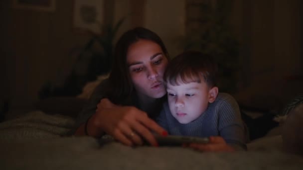 Heureuse mère de famille et fils couchés sur le lit dans la chambre de sa maison en jouant à des jeux l'écran de la tablette — Video