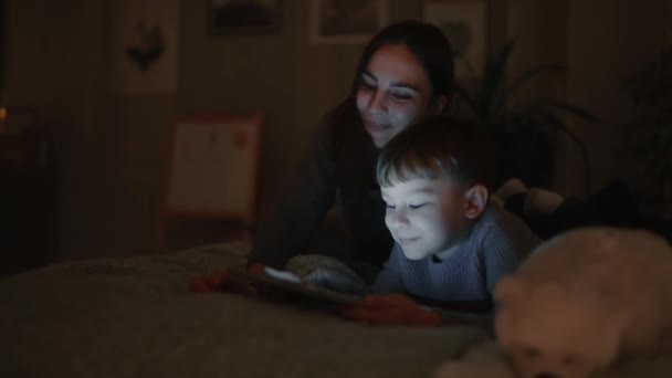 Lyckliga familjen mor och son ligger på sängen i sovrummet av hans hus spelar spel skärmen på surfplattan — Stockvideo