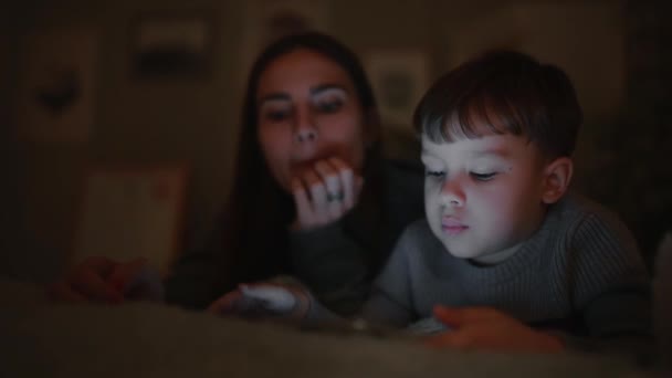 Glückliche Familienmutter und Sohn liegen auf dem Bett im Schlafzimmer seines Hauses und spielen Spiele auf dem Bildschirm des Tablets — Stockvideo