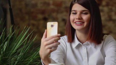 Kafede kahve yudumlarken akıllı telefon video sohbet konuşurken gülümseyen kız