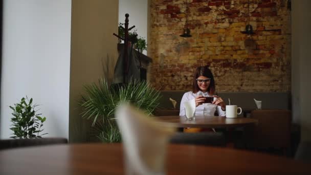 Smartphone flickan med app på telefonen dricka kaffe leende i café. vackra mångkulturella unga casual kvinnliga professionella på mobiltelefon. blandras asiatiska kaukasiska modellen. — Stockvideo