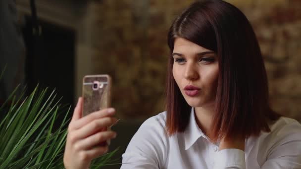 Usmívající se dívka v kavárně mluvit na video chat na chytrý telefon při pití kávy — Stock video