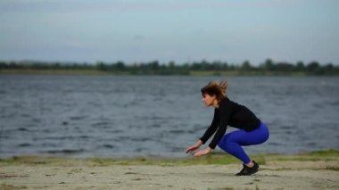 Güzel spor kız burpees akan Nehri yakınında sahilde atlama yok.