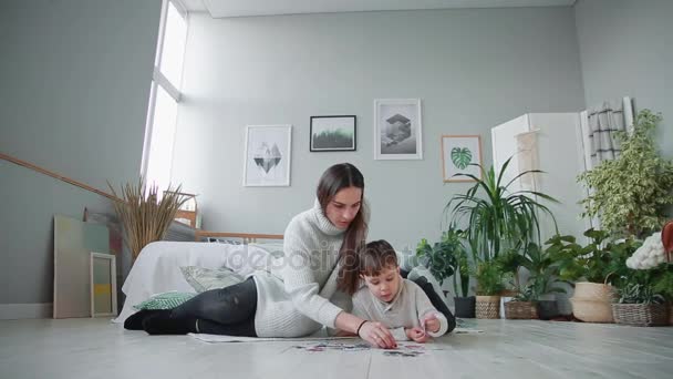 Mãe com uma criança no interior branco de sua casa para coletar o quebra-cabeça junto com seu filho. Família feliz, jogos educativos . — Vídeo de Stock