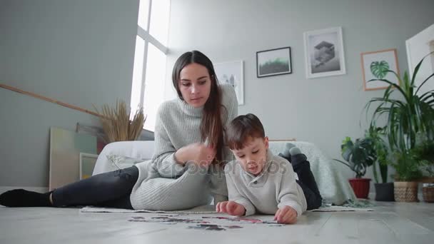 Madre con un niño en el interior blanco de su casa para recoger el rompecabezas junto con su hijo pequeño. Familia feliz, juegos educativos . — Vídeos de Stock