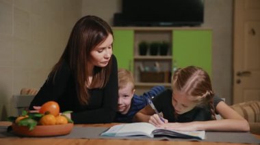 Küçük bir çocuk anne ve kızı bir okul ödevi yapıyor, izliyor. Kardeşim ödev yapmak için yardımcı olur.