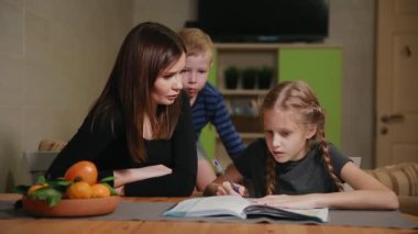 Küçük bir çocuk anne ve kızı bir okul ödevi yapıyor, izliyor. Kardeşim ödev yapmak için yardımcı olur.