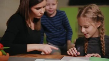 Küçük bir çocuk anne ve kızı bir okul ödevi yapıyor, izliyor. Kardeşim ödev yapmak için yardımcı olur.