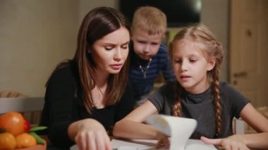Küçük bir çocuk anne ve kızı bir okul ödevi yapıyor, izliyor. Kardeşim ödev yapmak için yardımcı olur.