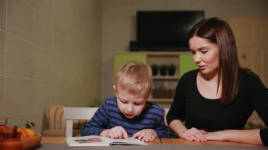 Anne ve oğlu evinin mutfağında oturan ve kitap okumayı öğrenme.