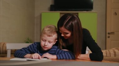 Anne ve oğlu evinin mutfağında oturan ve kitap okumayı öğrenme.