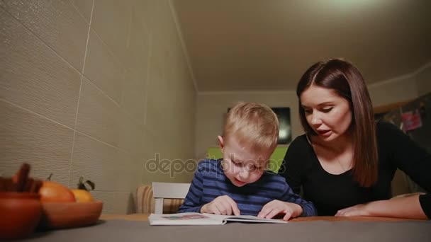 Mère et fils assis dans la cuisine de sa maison et apprenant à lire le livre . — Video