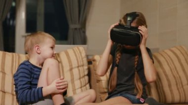 Kardeş kardeş evde ile sanal gerçeklik gözlükle oyun oynarken kanepede oturuyor. Mutlu bir aile