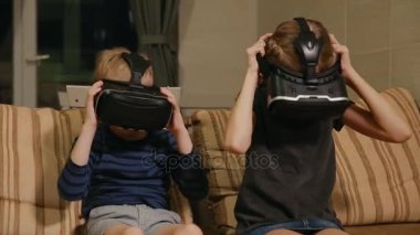 Kardeş kardeş evde ile sanal gerçeklik gözlükle oyun oynarken kanepede oturuyor. Mutlu bir aile