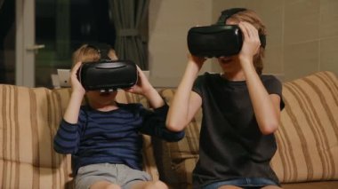 Kardeş kardeş evde ile sanal gerçeklik gözlükle oyun oynarken kanepede oturuyor. Mutlu bir aile