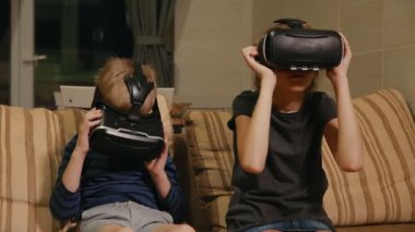 Kardeş kardeş evde ile sanal gerçeklik gözlükle oyun oynarken kanepede oturuyor. Mutlu bir aile