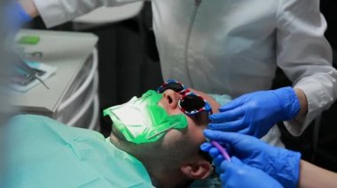 Diş hekimi ve hemşire hasta bir adamın bir diş tamiri. Matkap diş ve diş çürüğü ve sızdırmazlık kaldırmak için bormashenko kullanımı.