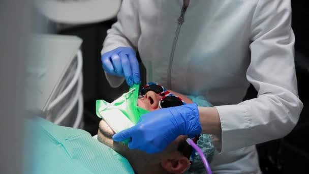 El dentista y la enfermera reparando un diente de un hombre paciente. El uso de bormashenko para taladrar los dientes y eliminar la caries dental y el sellado . — Vídeo de stock