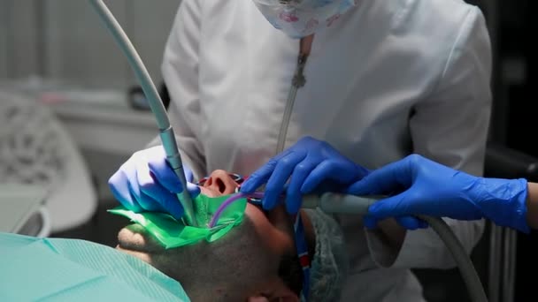 El dentista y la enfermera reparando un diente de un hombre paciente. El uso de bormashenko para taladrar los dientes y eliminar la caries dental y el sellado . — Vídeos de Stock