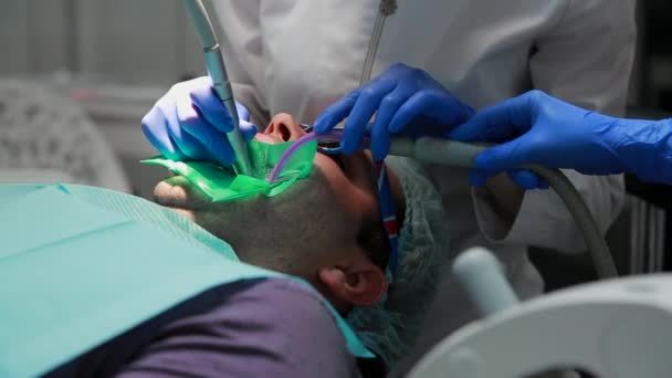 The dentist and nurse repairing a tooth of a patient man. The use of bormashenko to drill teeth and remove tooth decay and sealing. — Stock Video