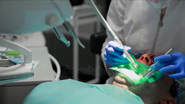 El dentista y la enfermera reparando un diente de un hombre paciente. El uso de bormashenko para taladrar los dientes y eliminar la caries dental y el sellado . — Vídeos de Stock