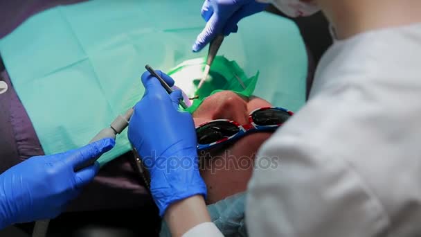 O dentista e a enfermeira a reparar um dente de um homem paciente. O uso de bormashenko para perfurar os dentes e remover a cárie dentária e vedação . — Vídeo de Stock