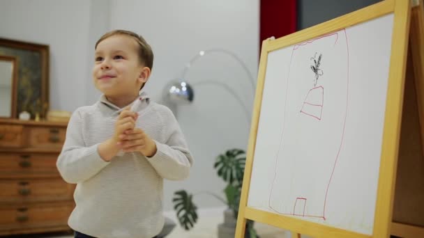 Het jongetje in de woonkamer van het huis vestigen op het bord met markers een childs tekening. Voorschools onderwijs. Close-up — Stockvideo