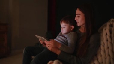 Güzel kadın anne evine oğlu ile çizgi tablet dokunmatik ekranda izlerken onun kucağına bir sandalyede oturuyor.