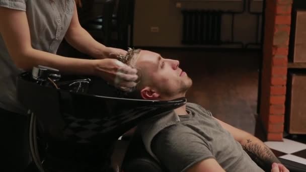 En kvinna tvättar håret i Barber shop skäggig man med schampo och balsam. Tvätta med schampo vattnet. — Stockvideo