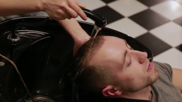 Een vrouw wast haar haren in de kapper winkel bebaarde man met shampoo en conditioner. De shampoo water afwassen. — Stockvideo