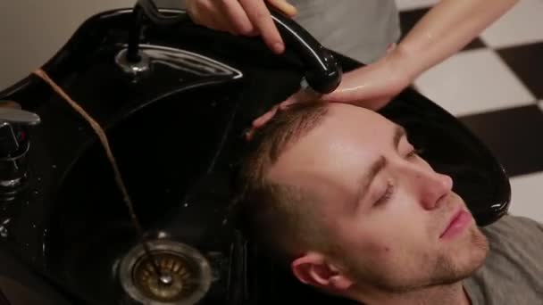 Женщина моет голову в парикмахерской бородатому мужчине с шампунем и кондиционером. Смой шампунь с воды. . — стоковое видео