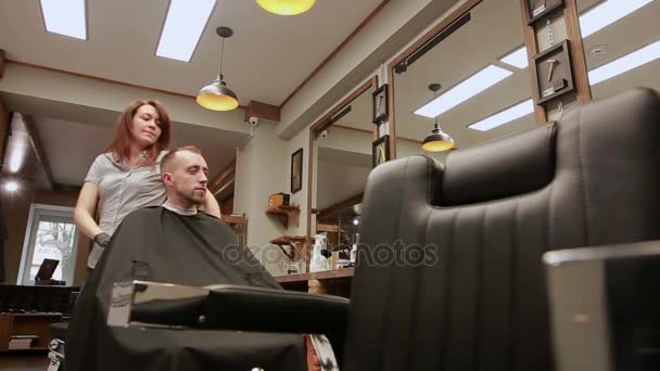 Una mujer barbero en la barbería para poner clientes hombre en una silla y comienza a llevar a cabo su corte de pelo. El valor — Vídeos de Stock