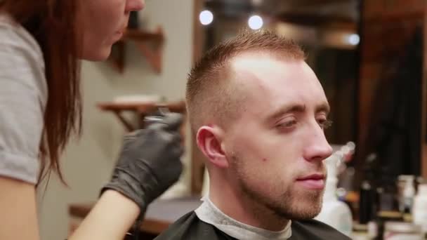 Uma mulher Barbeiro na barbearia para colocar os clientes homem em uma cadeira e começa a realizar seu corte de cabelo . — Vídeo de Stock