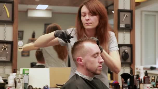 Een vrouw Kapper in de barbershop winkel om klanten man in een stoel en begint uit te voeren zijn kapsel. — Stockvideo