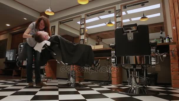 女性は、プロの美容師が椅子を下げるが、カメラは原始的な Hd ステディカム映像の助けを借りて移動します。理髪店で理容室を開始男を刃でシェービング. — ストック動画