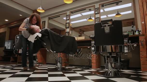 De vrouw is dat een professionele kapper verlaagt de stoel, beweegt de camera met de hulp van ongerepte Hd Steadicam beeldmateriaal. Kapper in de barbershop begint de man met het mes scheren. — Stockvideo