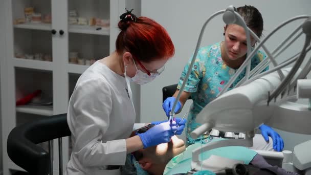 O dentista e a enfermeira a reparar um dente de um homem paciente. O uso de bormashenko para perfurar os dentes e remover a cárie dentária e vedação — Vídeo de Stock