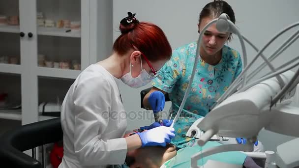 O dentista e a enfermeira a reparar um dente de um homem paciente. O uso de bormashenko para perfurar os dentes e remover a cárie dentária e vedação — Vídeo de Stock