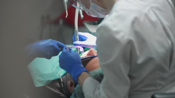 El dentista y la enfermera reparando un diente de un hombre paciente. El uso de bormashenko para taladrar los dientes y eliminar la caries dental y el sellado . — Vídeo de stock